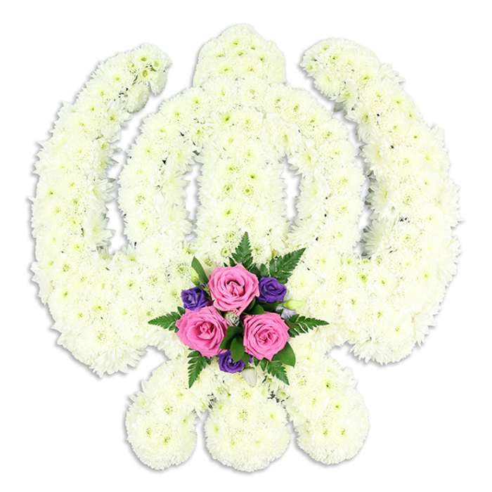In this image, a large Sikh Khanda floral tribute is presented in precise detail, set against a plain white backdrop that makes its symbolic form appear almost luminous. The Khanda shape itself is meticulously constructed from masses of white chrysanthemums, each small head nestled tightly into the next so that no foliage or framework shows through. The effect is a velvety, continuous surface that follows every curve of the chakkar and every edge of the central sword and twin kirpans. The chrysanthemums' slightly feathery petals create gentle texture, softening the bold outline of the emblem while still maintaining its clear religious significance. At the lower centre of the design, where the blades converge, sits a carefully composed accent posy. Three rounded pink roses, delicately unfurling, are framed by smaller, intense purple blooms-likely freesias or lisianthus-and sprigs of dark green fern. This contrast of colour adds depth and symbolism: white for peace, pink for love and gratitude, purple for dignity and devotion. The tribute appears to be resting upright, a subtle shadow underneath hinting at its three-dimensional presence. The overall mood is one of poised stillness, as though the arrangement has just been placed at the front of a service in Stanmore, ready to be viewed by gathered family and friends. The craftsmanship speaks of an experienced florist who understands both the technical demands of shaping such a complex symbol and the emotional weight carried by Sikh funeral flowers. It feels perfectly suited to a final farewell, a floral testament to faith, courage, and enduring memory.
