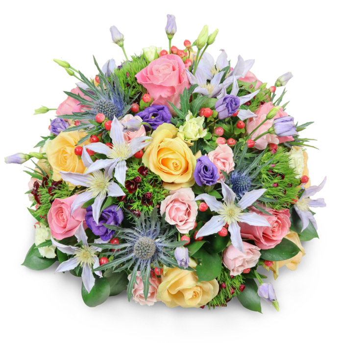 A lavish, dome-shaped bouquet of mixed flowers is captured against a bright white backdrop, the clean setting making every colour and texture clearly visible, much like a display piece in a Stanmore florist's window. The arrangement is densely composed yet appears airy, led by a profusion of garden roses in soft pink, creamy peach, and warm yellow tones. Some of these roses have fully opened into wide, layered rosettes, revealing gently curling petals, while others linger in mid-bloom, adding a dynamic, living quality to the design. Threaded among the roses are refined clematis blossoms in pale lavender and white, with slender, star-like petals radiating from yellow or white centres; these blooms bring a graceful, climbing-garden feel that recalls the quiet elegance of homes near Canons Drive. In deliberate contrast, several stems of blue eryngium, known as sea holly, stand proudly within the bouquet, their spiky, metallic blue-grey heads lending a distinctive, almost architectural texture that cuts through the softness of the surrounding petals. Deep purple lisianthus blooms weave through the arrangement in various stages, from tight buds to open, gently ruffled flowers, offering velvety pools of colour that intensify the overall palette. Bright red hypericum berries, clustered in small groups, glisten like tiny jewels, providing cheerful highlights and a crisp, rounded texture. The flowers are cradled by an abundant base of greenery, including broad, glossy leaves, finer feathery sprigs, and touches of dark, wine-shaded foliage that add subtle shadows and depth. Soft, even lighting accentuates the bouquet's round silhouette, casting only a delicate shadow beneath it. The composition feels warm, elegant, and uplifting, ideal as a celebratory centerpiece for a family gathering in Stanmore or as a thoughtful floral delivery marking a special moment near Queensbury and Edgware.