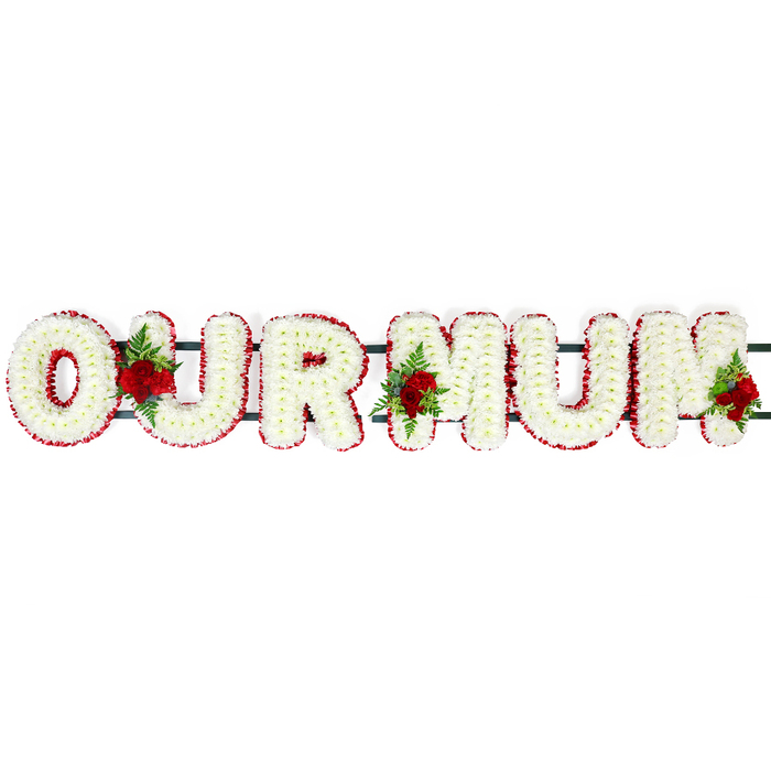 A tender and traditional OUR MUM funeral letter tribute is shown here, laid out horizontally on a pure white background that enhances every nuance of its form and colour. The letters are created in a bold block style, each one generously filled with dozens of white chrysanthemum heads. Their petals, tidy and slightly domed, interlock to form a dense, cushion-like surface, giving the words a softness that contrasts gently with the gravity of the occasion. Surrounding this white centre, a tight border of deep red flowers, likely spray carnations, traces the outline of each letter. The rich, velvety red provides a vivid frame that helps the message stand out clearly, while the petals' small ruffles add a touch of movement and life. Interspersed throughout the design are three small but expressive clusters of deep red roses, combined with sprigs of dark green foliage. One cluster appears in the gap between the O and U, another nestles between the U and the first M, and a final grouping graces the area near the second M. These roses introduce a focal element of passion and devotion, suggesting treasured memories and an unbroken bond with a beloved mother. Just visible beneath the flowers, a dark green horizontal structure links the letters together, suggesting a strong frame suitable for transport and display at a funeral or memorial service, perhaps at a Stanmore church, synagogue, or crematorium close to the town centre. The overall arrangement feels composed and deeply respectful, with the combination of white purity and red love conveying a message of gratitude and remembrance. It is easy to imagine this tribute placed carefully near the front of a service, quietly reflecting the gentle character and family values often felt around Stanmore's leafy streets and residential avenues.