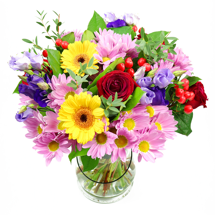 A generous, garden-style bouquet sits in a clear glass vase, carefully composed yet with a natural, slightly overflowing feel, photographed against a bright white background. At the centre, sumptuous deep red roses unfurl in dense spirals, their velvety petals catching soft light and giving the design a classic, romantic core. Nearby, radiant yellow gerbera daisies with dark, textured centres stand out boldly, their daisy-like heads reminiscent of little suns that instantly add optimism and joy. Around these focal blooms, layers of pink and lilac daisies or chrysanthemums spread outward, their many narrow petals and tiny yellow eyes forming a soft, feathery cushion that adds fullness and a gentle pastel haze. Woven through this cushion are graceful purple and lavender lisianthus stems, some in full bell-shaped bloom, others in bud, offering cool tones and elegant, ruffled curves that deepen the colour palette. Dotted between blossoms, clusters of bright red hypericum berries, smooth and round, provide playful pops of texture and a slightly festive touch. Lush greenery envelopes the flowers: broad, dark leaves give strength and structure, while slimmer, light-green sprigs soften edges and create a fresh, almost woodland feel, echoing the greenery surrounding local landmarks like Stanmore Hill and the open spaces around Brockley Hill. The transparent vase reveals the neatly spiralled stems and crystal-clear water, evidence of careful conditioning and expert floristry. Overall, the bouquet projects warmth, happiness, and thoughtful intention, making it an ideal choice for birthdays, anniversaries, thank-you gifts, or to bring a burst of colour and fragrance into homes and offices across Stanmore and the wider North West London area.