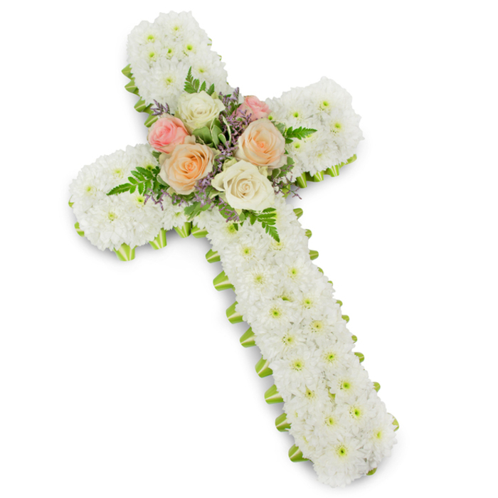 A large white floral cross dominates the frame, its classic shape set cleanly against a bright white studio background that emphasizes every subtle detail of the design. The cross is formed from a solid base and completely enrobed in clusters of white button chrysanthemums, placed so closely that they create a continuous, velvety surface with no gaps or visible foliage between them. This dense mass of blossoms gives the arrangement a soft, almost cushion-like appearance, making the symbol of the Christian cross feel gentle, approachable, and profoundly peaceful. Just at the margins, a slender ribbon of lime green peeks out from under the flowers, carefully secured along the perimeter to provide a crisp, defined border. The ribbon's fresh green tone introduces a quiet suggestion of new life and renewal without disturbing the calm predominance of white. At the intersection of the vertical and horizontal arms, a floral focal point brings a touch of colour and movement. Several premium roses in pastel tones-blush pink, creamy ivory, and light peach-are arranged in a small cluster, their multi-layered petals unfurling in soft spirals that catch the light. Fern fronds emerge from behind the roses, their fine, feathery texture adding depth and a gentle sense of outward expansion, while small sprigs of lavender-coloured filler blooms tuck into the spaces between petals, providing visual interest and a subtle hint of cool tone. This floral cross feels like a carefully considered tribute, suitable for a funeral or memorial service in Stanmore, perhaps resting near the front of a church or in the quiet of a crematorium chapel. It evokes the tranquillity of the nearby green spaces and the compassionate skill of experienced local florists who help families honour a loved one's memory with grace and sincerity.