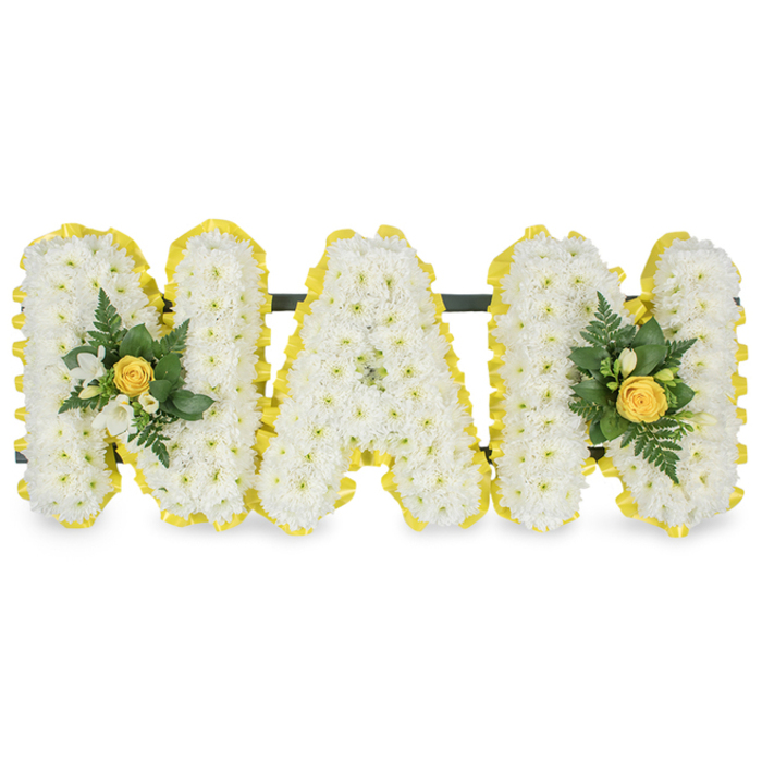 A vibrant, lovingly made floral tribute spells MAM in three individual capital letters, crafted as a tender token for a funeral service or graveside remembrance. Each letter is richly covered with fresh white chrysanthemum spray flowers, the tiny florets packed closely to create a plush, almost tactile surface that suggests both purity and solace. The perimeter of each letter is outlined in a bright yellow pleated satin ribbon, its pleats catching a soft, even light and providing a warm, uplifting edge against the pristine whites. Two elegant embellishments accent the piece: one nestles on the left upright of the first M, the other mirrors it on the right upright of the last M; each focal cluster features a tightly furled pale-yellow rose, encircled by small white freesia blossoms and set upon a spray of dark green fern fronds and glossy foliage that adds depth and a living contrast. A dark slender bar runs horizontally behind the top of the letters, offering unseen support so the tribute can be displayed steadily on an easel or placed at a graveside near Stanmore Park or the quieter streets by Bentley Priory. Photographed against a plain white backdrop, the design's delicate textures, soft colour palette and refined finishing convey a message of enduring affection, warmth and remembrance - the kind of arrangement a local florist would prepare with care for a family remembering a beloved mother.