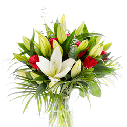 A boldly elegant white Oriental lily opens like a lantern at the heart of this bouquet, its pristine petals curving back to show pale yellow stamens and a tender green pistil that command attention. Encircling this central bloom are numerous lily buds in soft lime and buttery yellow tones - some tightly closed, others beginning to promise further bloom - creating a sense of unfolding life and graceful rhythm. Among these pale lilies, deep red rosebuds and small roses emerge like handwritten declarations of affection, their velvety crimson forms providing dramatic contrast against the lighter floral tones. The bouquet is richly layered with greens: large, glossy dark leaves give structure, while long, arching palm-like fronds in a fresh emerald hue add texture and a feeling of movement, as if a summer breeze has just passed through. Sprays of silvery eucalyptus, recognisable by their round, muted leaves, offer cool tonal relief and a discreet, aromatic counterpoint. All of this sits in a clear, cylindrical glass vase so simple it lets the stems and water speak - pale green shafts visible through sparkling liquid under bright studio light, emphasising the arrangement's freshness. The white background gives the composition a clinical clarity that highlights textures and colour interplay; you can almost smell the lilies' sweet, powdery scent mingling with the roses' deeper perfume. Created with the care of a local Stanmore florist, this design would make an elegant gift for romance, celebration, or quiet sympathy, and is arranged with the same attention to seasonal freshness and delivery reliability customers expect in Stanmore and the surrounding streets near Stanmore station and Canons Park. Flower Delivery Stanmore prepares bouquets like this for local delivery with care and local knowledge.