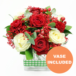 This image shows a sophisticated floral arrangement set cleanly against a white backdrop, allowing every colour and shape to stand out. At the centre, velvety red roses with gently unfurling petals are paired with creamy white roses, whose ivory tones soften the overall palette and lend a serene glow. The interplay of crimson and cream is both romantic and timeless, evoking an elegant dinner table in a Stanmore home not far from the tree-lined streets around Gordon Avenue or the calm of Bentley Priory Nature Reserve. In between the roses, wisps of fine red filler flowers, similar to dyed baby's breath, create delicate, cloud-like clusters that give the bouquet a light, airy quality. Scattered through these are smooth red hypericum berries, rounded and highly polished, adding bright points of shine and a cheerful, festive energy. Around the main blooms, eucalyptus leaves and assorted green foliage arc and curl, their varied shades of green and soft blue-green silhouettes giving the composition depth and movement, as if gently stirred by a breeze. The flowers are arranged in a contemporary rectangular glass vase, the clear sides revealing straight, cleanly cut stems that testify to expert preparation by local florists. A green and white gingham ribbon wraps horizontally around the vase, adding a touch of rustic charm that feels both fresh and homely, ideal for a Stanmore kitchen table or hallway console. Positioned in the bottom right corner of the image is an orange circular graphic with the words "VASE INCLUDED" written in bold white font, making it immediately obvious that the bouquet arrives complete and ready to place, suited to anniversaries, romantic gestures, or thoughtful deliveries across Stanmore and neighbouring areas.