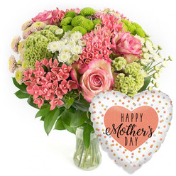 This photograph shows a joyful Mother's Day arrangement that feels both classic and fresh, much like the relaxed elegance of homes around Stanmore Hill. Set against a pure white background, the bouquet occupies the left side of the frame in a rounded, balanced shape, resting in a clear glass vase that reveals the stems and water within. The main focal flowers are pink roses, their blooms fully open but still crisp at the edges, petals layered in gentle spirals with a slightly deeper pink along the rims. Around and between these, mounded clusters of coral-pink flowers, reminiscent of kalanchoe, add intricate detail and a sense of abundance, every tiny blossom contributing to a rich tapestry of colour. Lime-green button chrysanthemums punctuate the pinks with vivid, almost zesty dots of colour, their tight, tufted heads offering a fascinating, textured contrast. Threaded throughout the arrangement, little white spray chrysanthemums with daisy-like faces introduce brightness and space, preventing the palette from feeling too dense and instead giving the bouquet an airy, uplifting quality. The flowers are supported by a framework of dark green foliage, the leaves arching outward and upward to cradle the blossoms, enhancing the rounded silhouette and grounding the lively colours. The simple glass vase allows the natural stems to be part of the visual story, adding a sense of honesty and freshness. To the right, a heart-shaped foil balloon shimmers gently, its white background scattered with metallic dots in gold, silver, and peach that catch the light. In the centre, a soft peach heart holds the phrase "HAPPY Mother's DAY" in an attractive mix of bold and script-style black lettering. The whole scene suggests a carefully chosen Stanmore flower delivery, waiting on a dining table, perhaps in a home just off The Common, ready to bring a smile to a much-loved mum.
