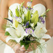 A refined bridal bouquet that captures a bright, hopeful wedding morning in Stanmore: broad, star-shaped white lilies dominate the arrangement, their velvety petals unfolding to reveal pale anthers and a soft internal glow as if lit by early daylight. Interspersed are lisianthus blooms with purple-tinged edges, each ruffle offering a painterly contrast that gently defines the bouquet's shape. Small clusters of baby's breath and the whisper-fine stems of maiden grass thread between the larger blooms, lending a demure, lacy texture that softens the overall composition. Delicate veronica spikes provide subtle vertical accents, adding rhythm and a slender depth that keeps the eye wandering. The greenery is a crafted mix of matte and glossy leaves, creating a natural frame that lifts and supports each flower while introducing a cool green backdrop to the warm creamy whites and cool violets. The scent is quietly intoxicating - lily sweetness balanced by dewy, grassy notes that bring to mind a walk through Stanmore Common at dawn. Each stem is chosen and layered with experienced care so the bouquet reads as both harmonious and intentional, comfortable to carry and memorable in photographs. As a local florist I imagine this bouquet complemented by a ceremony near Canons Park or delivered for a reception on Stanmore High Street; Flower Delivery Stanmore would prepare it with the same attention to freshness and composition that readers expect from our neighbourhood floristry.