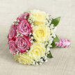 A beautifully constructed rose bouquet lies gently on a soft, beige-toned background, its subtle woven texture giving the impression of a natural linen cloth laid out for a special occasion. The bouquet itself is round and hand-tied, with a precisely balanced palette: on one side, rich magenta-pink roses cluster together in a dense, velvety sweep of colour; on the other, smooth, creamy yellow roses open wide, their petals unfolding in spirals that feel both luxurious and inviting. Threading through both sections are fine, cloud-like sprays of white gypsophila, or baby's breath, creating a dreamy, almost ethereal veil around the more substantial rose heads. Here and there, a few deep green leaves edge out from the blooms, giving the composition definition and a gentle nod to the garden origins of each stem. The stems beneath are gathered with care into a neat handle, tightly wrapped in glistening pink satin ribbon that shines softly against the neutral background. A slim strand of white pearls winds upward around the handle in a delicate spiral, adding a sense of bridal refinement often seen at Stanmore weddings, from intimate ceremonies near Stanmore Hill to larger gatherings close to Canons Park. The lighting in the image is calm and flattering, enhancing the bouquet's romantic colours without harsh shadows. The overall impression is of a thoughtfully designed bridal or anniversary bouquet, crafted by local experts who understand how roses, texture, and small details can transform a moment, whether it's a walk down the aisle or a surprise same-day delivery to a loved one's doorstep in Stanmore.