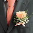 Subtle and sophisticated, this Stanmore buttonhole is a floral testament to love, tradition, and the quiet beauty of life's milestone moments. At its heart, a single rose in soft peach hue emerges in elegant detail, each petal gently unfurling as if inspired by the warm embrace of a Stanmore sunset. The bloom is delicately framed by clouds of airy white gypsophila-baby's breath-which lend the arrangement a dreamy softness reminiscent of early mornings wandering through Canons Park. Trim, vivid sprigs of green and a single broad leaf arc gracefully, infusing the composition with freshness and gentle movement. The suit's charcoal fabric forms a crisp, dignified background, while a peach satin ribbon, meticulously tied in a petite bow, unites the floral stems with refined polish and mirrors the coral tones of the expertly tied necktie beneath. Every detail is the work of skilled hands familiar with Stanmore's celebratory traditions, ensuring the boutonniere is more than an accessory-it is a keepsake that marks the wearer's place in the heart of the moment. Crafted by local florists and available for same-day delivery around Stanmore and its neighbouring lanes, this boutonniere brings quiet grace and a celebration of unity to wedding days, proms, and any event where love and memory are meant to bloom.