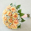 This arrangement is a portrait of tenderness: a clustered bouquet of soft peach roses whose creamy, layered petals fold toward one another, forming a rounded, intimate silhouette. Interlaced among the roses is a generous halo of white gypsophila, each tiny bloom dancing between the larger roses and creating a dreamy, cloudlike surround that lightens the composition. Broad, deep-green leaves provide a lush, structured backdrop, their glossy surfaces offering contrast and depth while guiding the eye inward. The stems are meticulously wrapped in a peach satin ribbon studded with pearl details, the tactile finish lending a refined, almost heirloom quality that feels perfectly suited to a wedding, anniversary, or vow renewal. Shot in gentle daylight with a soft, neutral setting, the bouquet reads as both modern and timeless; the lighting reveals subtle apricot undertones and the velvety textures of the petals. The scent is understated and fresh: soft rose fragrance tempered by green, leafy notes and the faint sweet breath of gyp. As a local florist regularly delivering to brides and families around Stanmore Station, Bentley Priory, and the lanes near Harrow-on-the-Hill, I picture this bloom cradled on a walk through Stanmore Common or carried down a church aisle in The Broadway. Flower Delivery Stanmore prepares stems with that same attention to balance and comfort, ensuring the bouquet sits naturally in the hand and photographs beautifully. It evokes anticipation and joy, a tactile keepsake of a day marked by care and quiet celebration.