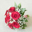 Resting on an off-white, textured surface that calls to mind a linen runner on a Stanmore dining table, this hand-tied bouquet exudes classic romance. At the centre, a compact cluster of deep crimson red roses is in full bloom, with petals that appear velvety to the touch, opening in perfectly layered spirals that speak of devotion and affection. Intertwined amongst the roses, delicate strands of gypsophila-baby's breath-form a halo of crisp white, each minuscule flower like a tiny star dotting the night sky, softening the boldness of the red and adding an ethereal, cloud-like surrounding. Around the edges, smooth, dark green leaves, possibly ruscus or similar foliage, peek from beneath the blossoms, creating a lush green frame that anchors the design and brings to mind the well-kept gardens and tree-lined roads around Canons Drive or Stanmore Hill. The stems are gathered tidily below, cut to an even length and bound in a rich red ribbon that matches the roses, finished with a spiral or stripe of small white pearl-like beads that run along the handle, lending the bouquet an elegant, ceremonial feel. Against the neutral background, the colours appear rich and balanced rather than overpowering, allowing every detail to be appreciated. This arrangement feels ideal for a wedding procession in Stanmore, an anniversary surprise at home, or a special delivery across nearby areas such as Edgware or Harrow, capturing both the sophistication and warmth often associated with meaningful celebrations.