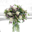 Gently illuminated as though set near a wide, sunlit window in Stanmore, this sympathy bouquet stands in a clear glass cylindrical vase, offering a calm and dignified presence. The arrangement is led by creamy white roses, their petals thick, soft, and perfectly arranged, each bloom unfurling with an air of tenderness and respect. Tucked between the roses are graceful stems of alstroemeria, their petals painted in subtle shades of mauve, lilac, and quiet purple, with touches of green that hint at the leafy landscapes around Stanmore Country Park and the nearby residential gardens. Throughout the bouquet, fine tufts of white baby's breath appear like tiny clouds, gently bridging the spaces between larger flowers and giving the whole design a light, airy feeling. Encasing the blooms is a generous collection of rich, glossy greenery, with both broad leaves and slender stems working together to lend structure and a sense of grounded calm. The glass vase reveals the tidy bundle of green stems immersed in clear water, reinforcing the bouquet's fresh, natural character. Behind the flowers, the bright, softly diffused white background suggests a serene indoor setting, free of distractions and filled with gentle light that makes every colour appear clean and pure. The bouquet carries an atmosphere of quiet solace and understated elegance, ideal for expressing sympathy or offering a thoughtful tribute in Stanmore, Queensbury, and the surrounding areas. Arranged by experienced local florists, it serves as a gentle, living message of care, support, and remembrance when words are difficult to express.