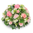 A soft, dome-shaped sympathy tribute photographed against a pure white backdrop, carefully composed of lush pink roses and clusters of pristine white freesia with a cushion-like silhouette. The dominant roses range from fully opened, velvety blooms in gentle blush and warm salmon tones to smaller spray roses whose tightly layered petals add depth and intimacy; they read as classic, comforting focal points. Interspersed are upright stems of white freesia, some showing their delicate, bell-shaped faces with pale yellow stamens and others still tightly furled, their scent almost imaginable in the warm, natural light that grazes the petals. A rich palette of greenery-broad, glossy dark leaves (the kind of ruscus or salal a local florist would choose) sits beneath, while variegated leaves edged in cream (reminiscent of pittosporum) give the design a soft brightness and a gentle contrast. The arrangement is densely packed so no stems are visible, creating a formal, refined cushion that would sit naturally at a memorial service or sympathy table. The texture moves from the plush rose heads to the crisp, slightly waxy foliage, and the overall feeling is of quiet comfort and considered craft. As a florist who often delivers to services near Stanmore High Street, Canons Park chapel, and the quieter corners of Stanmore Common, I picture this piece set beside a framed photograph or on a low pedestal, its understated palette meant to soothe and honour, rather than to claim attention. The subtle shadow on the white surface and the soft morning light highlight the arrangement's serenity and the florist's careful, compassionate touch.