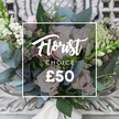 A handcrafted, hand-tied bouquet arranged in a loose, garden-picked style, resting on an ornate, distressed cream console that hints at timeless elegance. The composition is centred on soft blush garden roses with full, unfurling petals whose velvet texture contrasts with the crisp, silvery-blue eucalyptus leaves fanning outward. Small clusters of bright white berries-snowberry-like in form-dot the arrangement, catching the light and adding a cheerful, tactile brightness between sprays of tiny white filler flowers that resemble waxflower or astrantia. Subtle touches of deeper pink and burgundy buds nestle in the shadows, lending depth and a warm counterpoint to the pale palette, while taller green-and-white spikes peek from the left and right edges, giving vertical movement reminiscent of snapdragons. A cream satin ribbon binds the stems into a relaxed yet refined hand-tied finish, its soft sheen echoing the muted daylight falling across the scene. The overall mood is understated luxury: romantic, soothing, and quietly celebratory-ideal for birthdays, anniversaries, or simply to lift a kitchen table with seasonal charm. The scent is imagined as a calming eucalyptus coolness with a hint of sweet rose, and the varied textures invite a gentle touch from velvety petals to the slight prick of foliage. Captured in soft, natural light against carved plaster detailing, the bouquet reads as both accessible and bespoke-a trustworthy 'Florist Choice' style that suggests a local artisan's attention to seasonal freshness and thoughtful composition in Stanmore homes and Hampstead gardens alike.